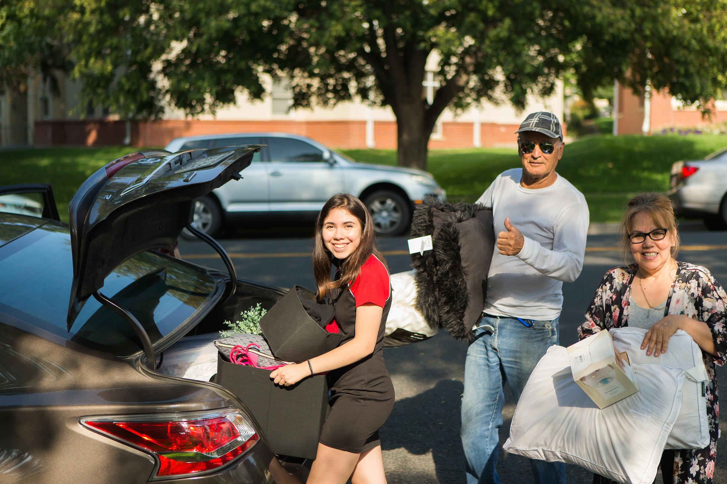 People pose while getting luggage out of the trunk of their car.