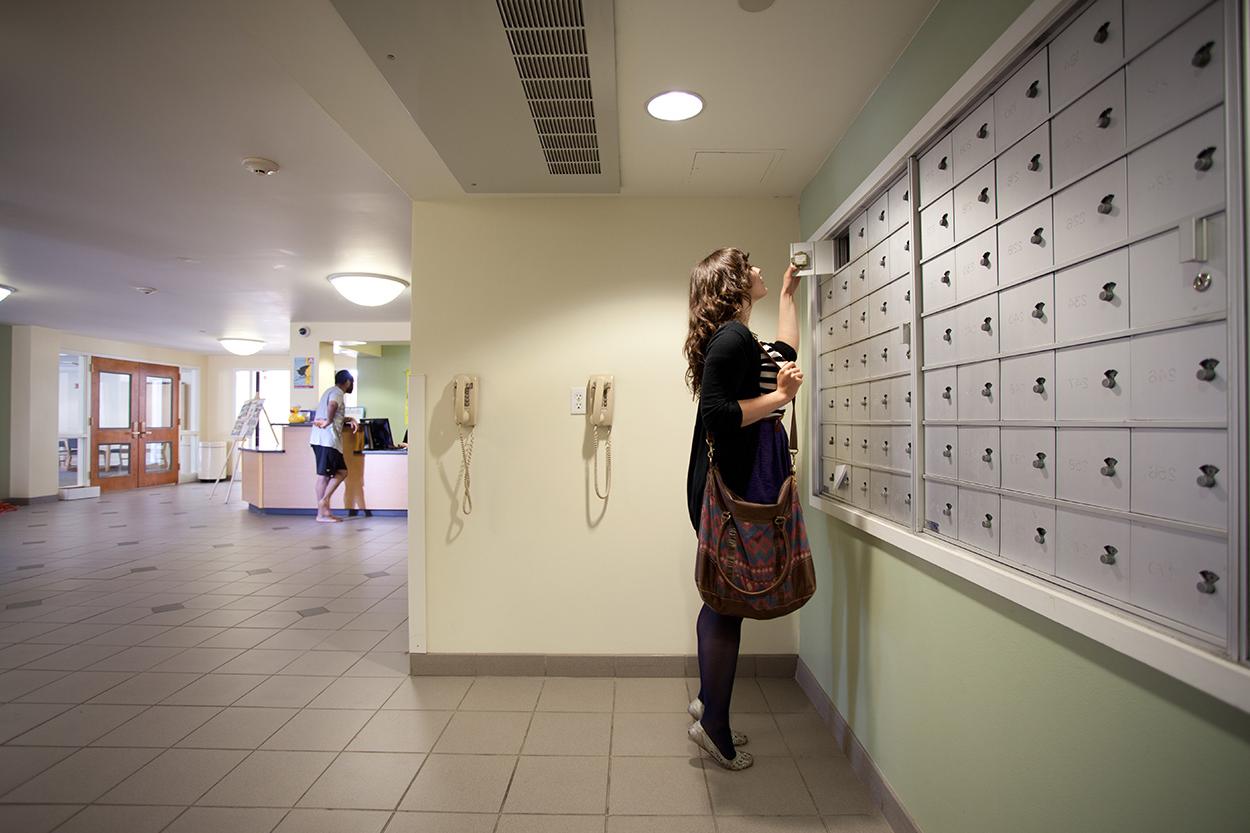 Student looks inside mailbox in the mailroom.